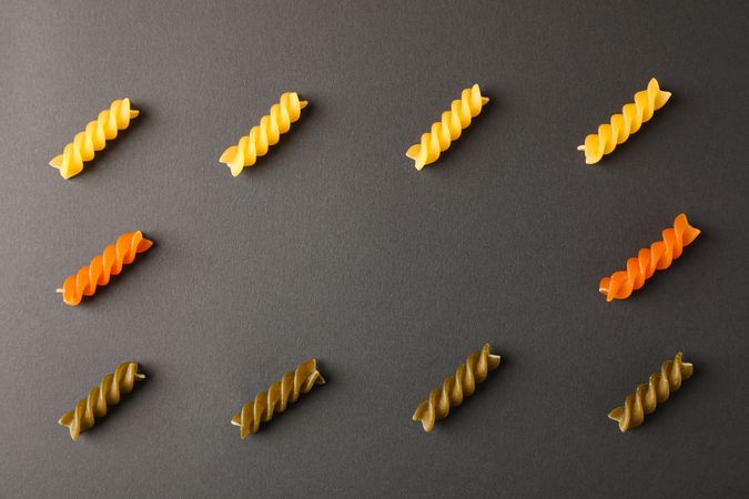 Flat lay composition with multicolored pasta on dark background, space for text