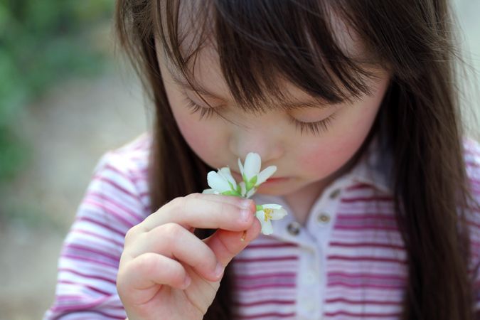 Portrait of young girl with Down syndrome smelling a flower in the park