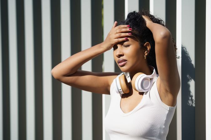 A woman wearing a tank top and headphones thoughtfully faces challenges in the outdoors