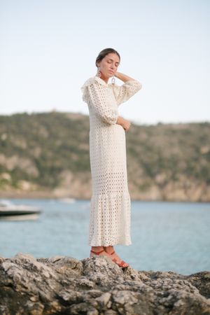 Gracious young woman standing on rocky cliff over sea with closed