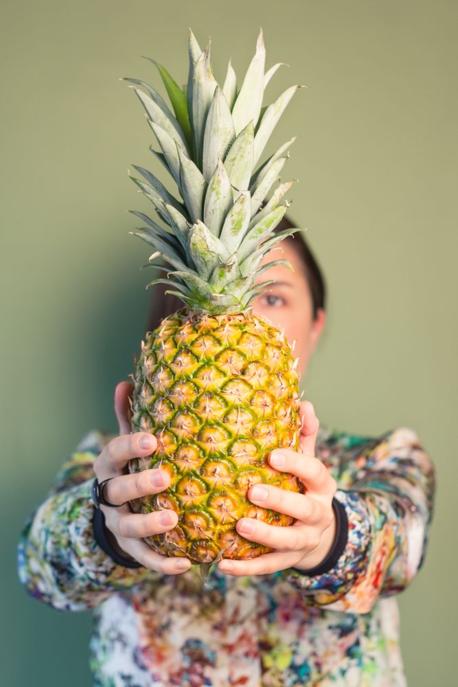 Woman holding pineapple in front of face