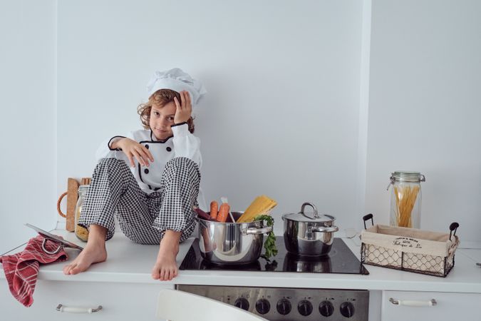 Adorable preteen boy in chef uniform sitting on kitchen counter