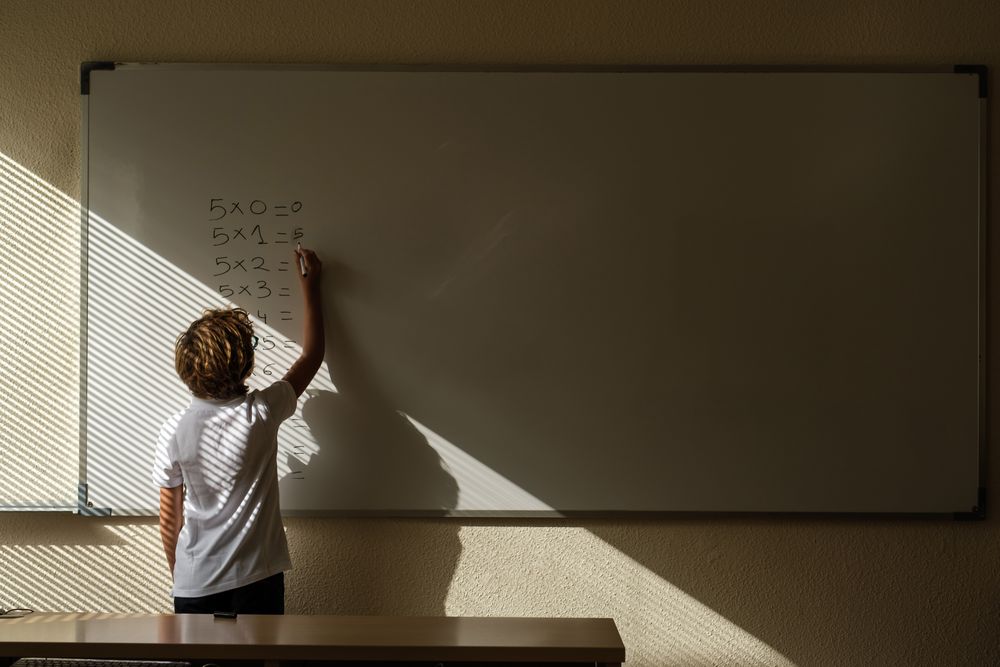 Unrecognizable schoolchild writing on whiteboard during math les