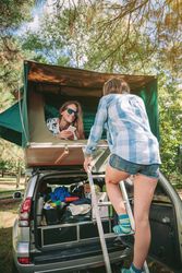 Woman ascending up ladder to tent over car