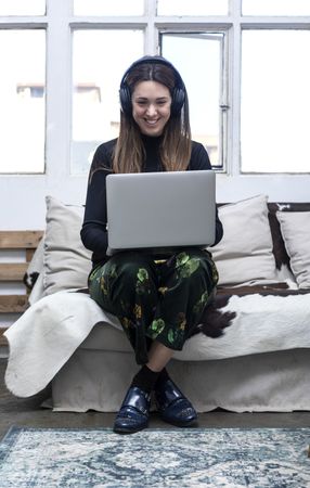 Woman sitting on sofa and using laptop listening to headphones