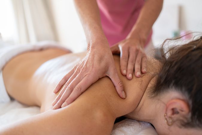 Close up of hands of masseuse working on client's shoulders