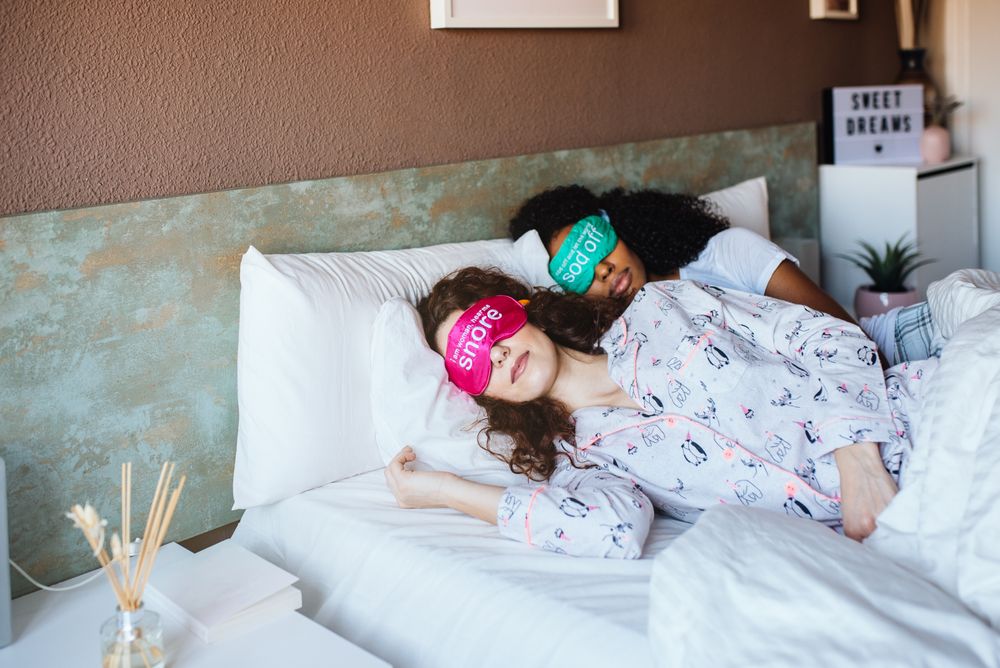 Female friends relaxed sleeping in bed with blindfold at home