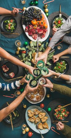 Group toasting at festive table with candy canes and roasted pears, vertical composition
