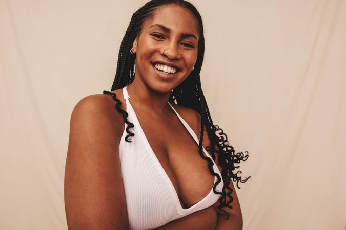 Confident woman with braids and piercings smiling and looking at the camera in a studio