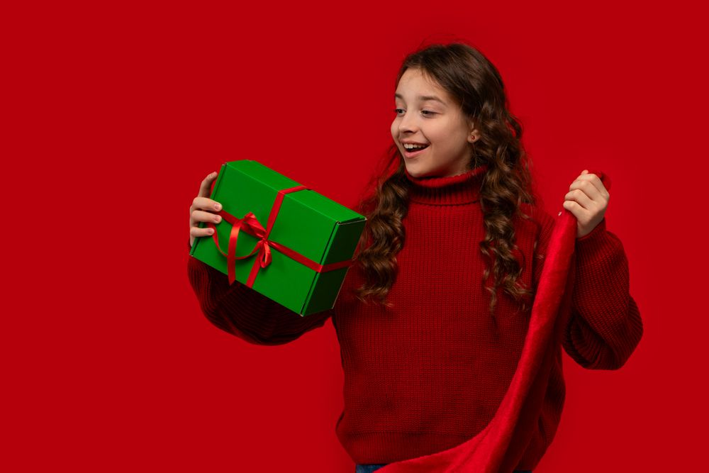 Excited girl holds Christmas gift and Santa hat.