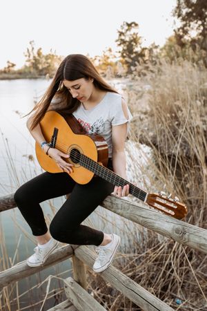 Young woman playing guitar near water