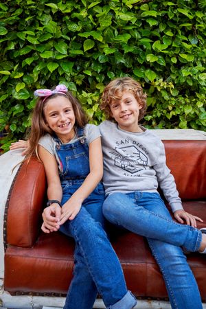 Cheerful siblings sitting on leather sofa in park