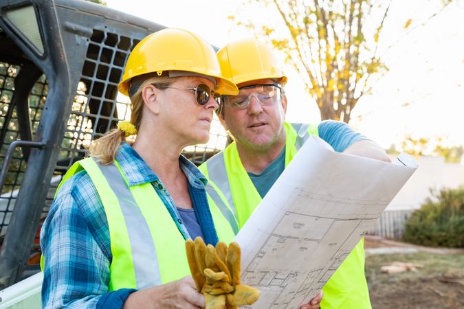 Male and Female Workers With Technical Blueprints Talking at Construction Site