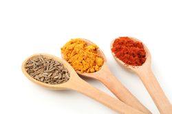 Three wooden spoons with earthy spices on plain background