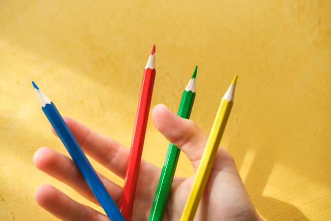 A child's hand picking up coloured pencils on a yellow backgroun