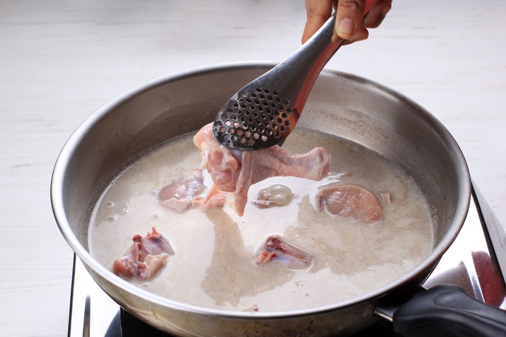 Female Hand Add Chicken Thigh Drumstick to the Pan using Tongs, Making Indonesian or Thai Style Curry