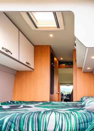 Bed with green linen inside of empty motorhome, vertical