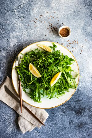 Top view of healthy vegetable salad with organic arugula, lemon and flax seeds on stone background, vertical composition