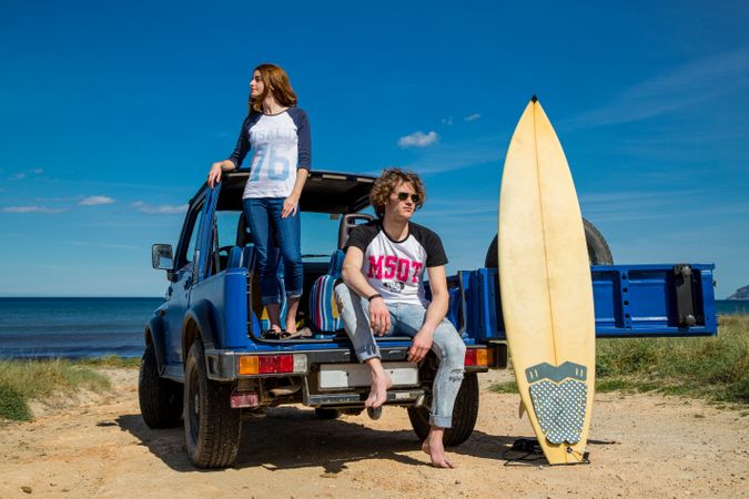 Guy with surfboard and woman standing on car