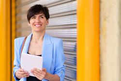 Smiling woman in blue blazer standing outside of shutter with digital tablet