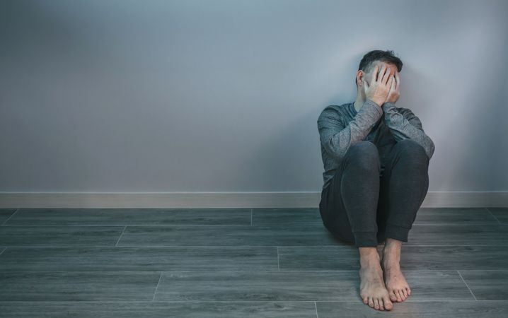Man crying while covering his face with hands sitting on the floor