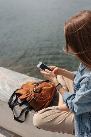 Top view of woman sitting on a ledge using a smarthphone