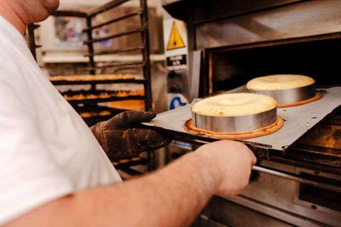 Male baker putting cakes into oven