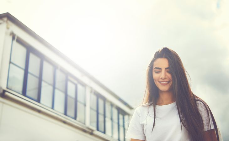 Brunette woman looking down and smiling walking past a building outside