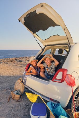 Children inside the trunk of a car making joke gestures with bas