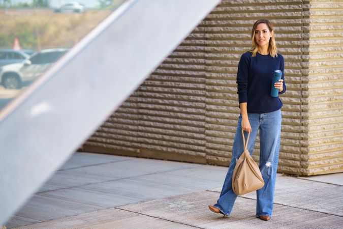 Stylish female standing on street with thermos and bag