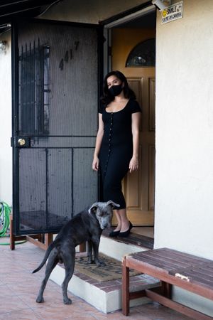 Confident woman standing in front of her house looking at camera with dog nearby