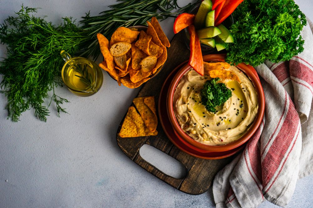 Top view of hummus dish on cutting board with chips and fresh veggies
