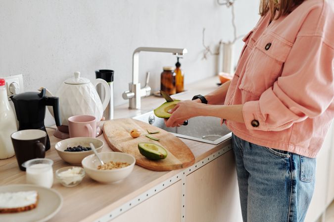 Cropped image of woman pealing an avocado standing beside kitchen counter