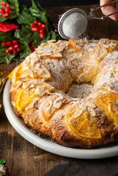 Person dusting powdered sugar over a cake with orange slices