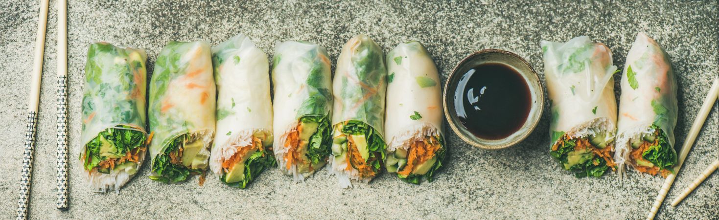 Vegetarian spring rolls lined up in a row with dipping sauce and chopsticks