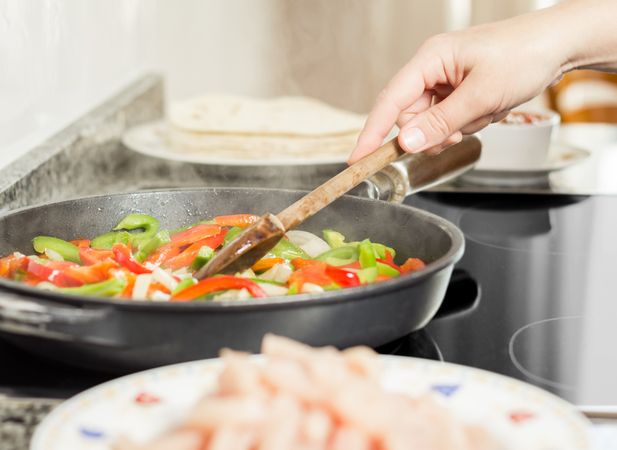 Female cooking vegetables and chicken in pan