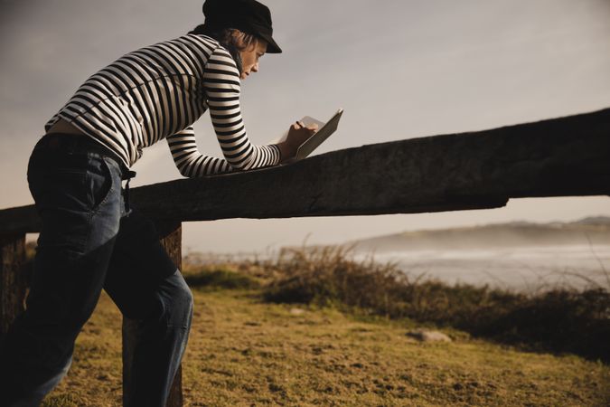 Woman writing in notebook and leaning on bench on shore near water