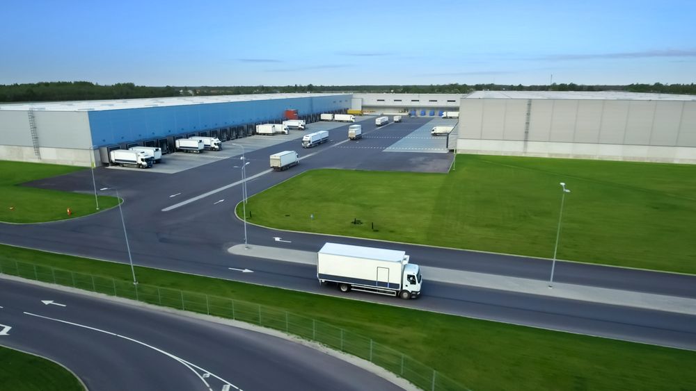 Trucks Navigate a Modern Warehouse Complex, Showcasing Efficient Logistics and Streamlined Cargo Operations Under a Clear Blue Sky