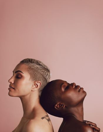 Side view of two diverse women against each other over beige background with copy space