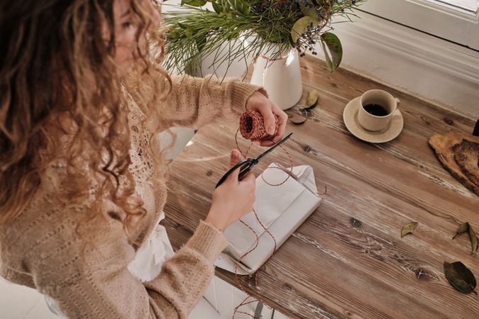 Crop female preparing for event and decorating gift with red rop