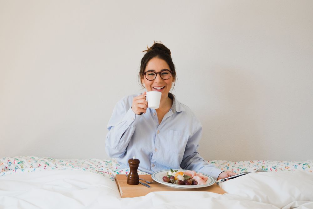 Young woman with breakfast on bed using smart phone