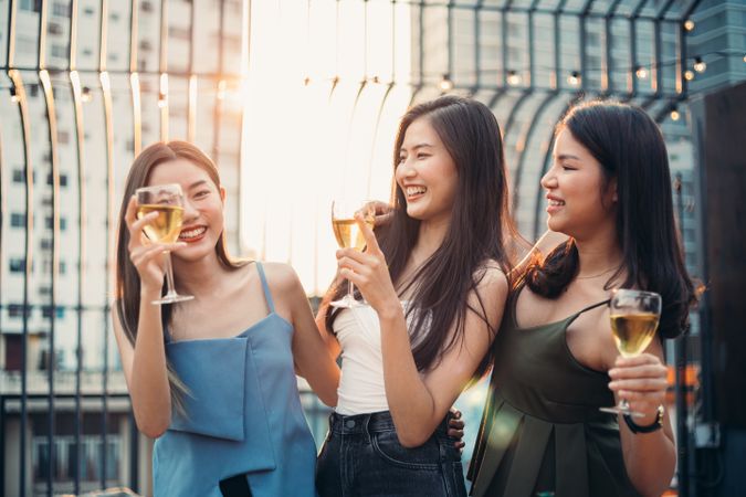 Group of Asian women drinking glasses of wine and dancing together