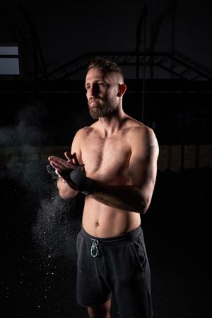 Shirtless sportsman clasping hands in dark room