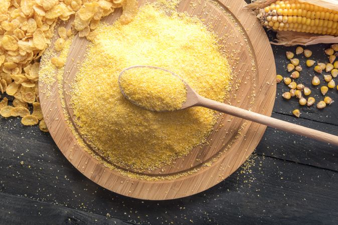 Cornmeal and cereal flakes on a wooden plate with a spoon in the cornmeal on a wooden table