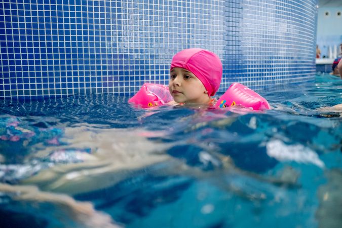 Cheerful girl in hat smiling and swimming in pool in water park