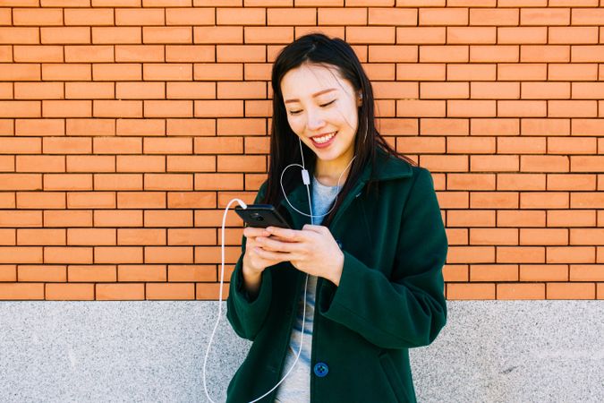 Asian female listening to music near brick wall