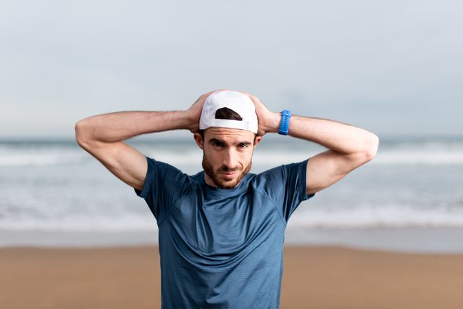 Confident male gymnast in active wear and cap on beach