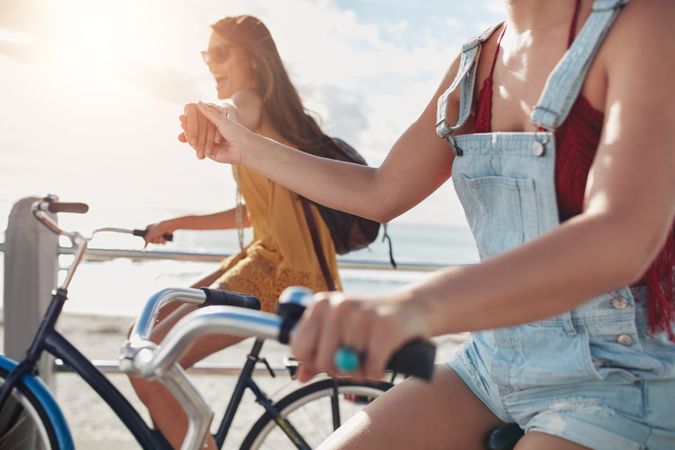 Two female friends holding hands and riding cycles on the seaside promenade