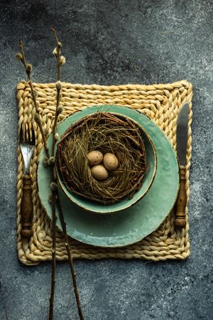 Top view of Easter holiday table setting with eggs in nest on grey counter