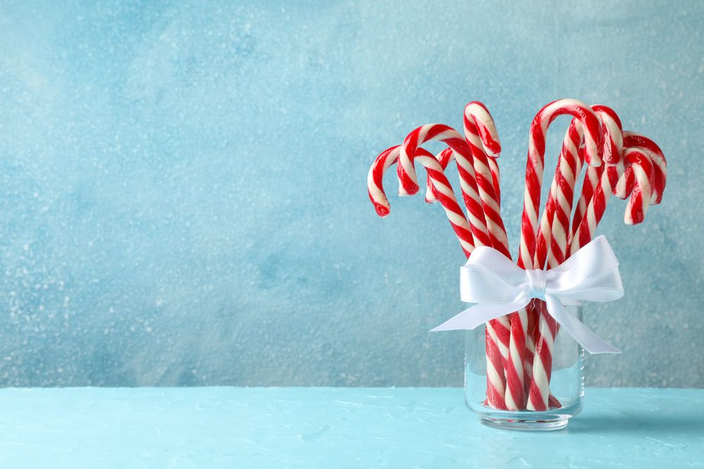 Candy canes in glass jar on blue background, space for text